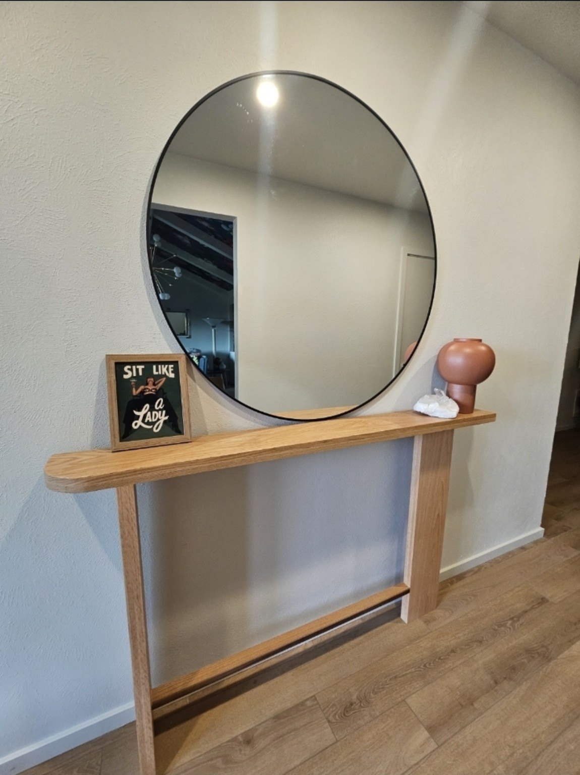 Custom narrow wood console beneath a round mirror